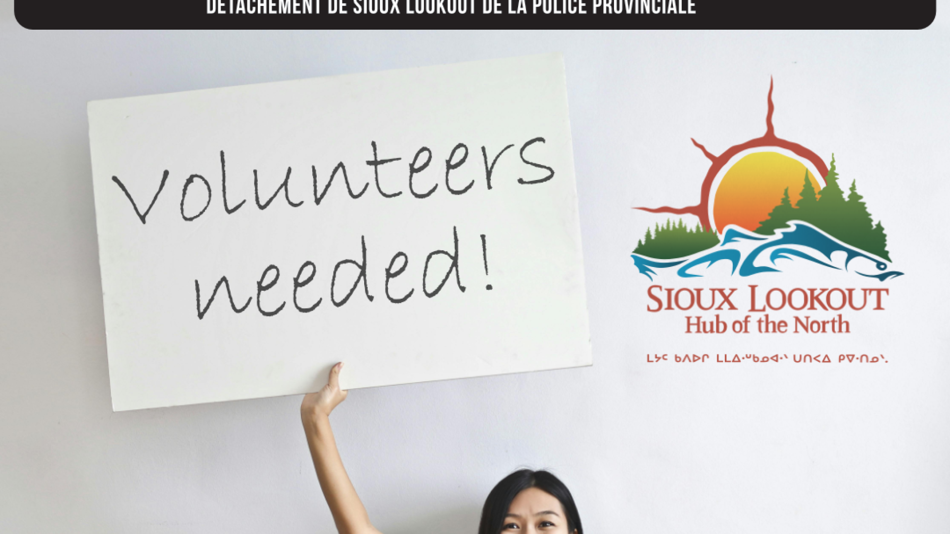 Woman holding up a sign that reads volunteers needed